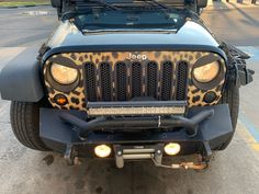 the front end of a leopard print jeep with its hood up and lights on, parked in a parking lot