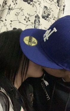 a person wearing a blue hat kissing another person's face while sitting on a couch