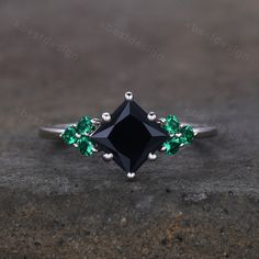 a black diamond ring with green stones on it's sides, sitting on top of a concrete surface