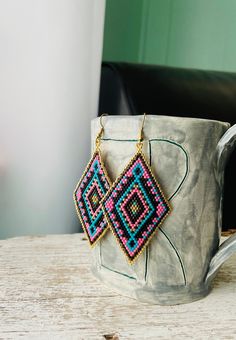 a pair of beaded earrings sitting on top of a white cup next to a black chair