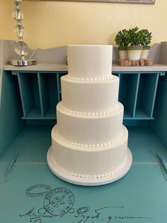 a three tiered white cake sitting on top of a blue counter next to a potted plant