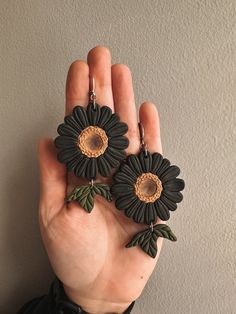 a hand holding two black and green flower earrings