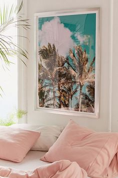 a bed with pink sheets and pillows in front of a palm tree print on the wall