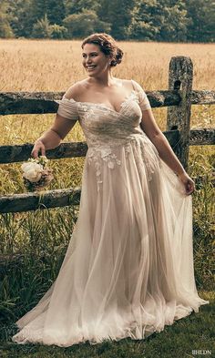 a woman standing in front of a wooden fence wearing a dress with flowers on it