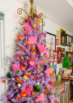 a brightly colored christmas tree in a living room with pictures on the wall behind it