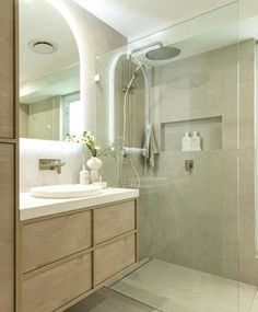 a bathroom with a walk in shower next to a white sink and wooden cabinetry