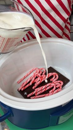 chocolate and candy canes are being poured into a slow cooker with milk in it