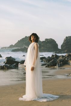 a woman standing on top of a sandy beach next to the ocean wearing a white dress