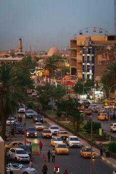 a city street filled with lots of traffic next to tall buildings and palm trees on both sides