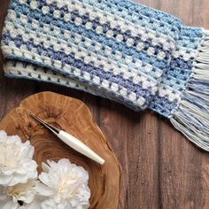 a crocheted blue and white blanket sitting on top of a wooden plate next to flowers