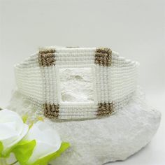 a white beaded bracelet sitting on top of a rock next to a flower bouquet