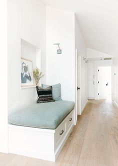 a room with white walls and wood floors has a day bed in the corner, along with a painting on the wall