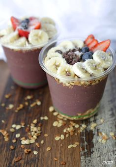 two cups filled with fruit and granola on top of a wooden table