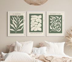 two green and white art prints hanging on the wall next to a bed with pillows