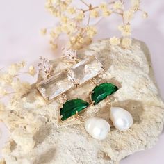 two pairs of green and white earrings sitting on top of a rock next to flowers