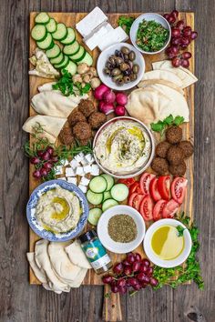 an assortment of food is laid out on a cutting board with olives, cucumbers, and pita bread