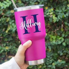 a person holding up a pink tumbler with the letter i on it