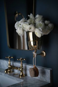 white flowers are in a vase hanging from a brass holder on a marble countertop