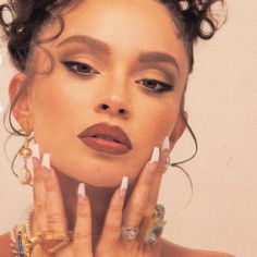 a woman with her hands on her face, wearing rings and earrings in front of her face