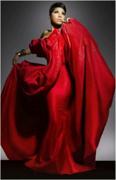 a woman in a red dress is standing with her arms on her hips and she's wearing a cape