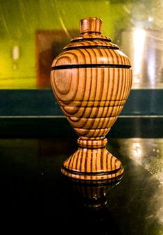 a wooden vase sitting on top of a black table next to a green and yellow wall