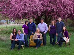 a group of people posing for a photo in front of a tree with purple flowers