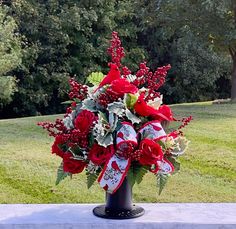 a vase filled with red and white flowers on top of a cement slab in front of trees