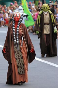 two people dressed in costumes walking down the street with other people watching from behind them