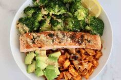 a white plate topped with broccoli and fish next to a bowl of pasta