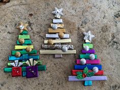 three small christmas trees made out of wooden sticks and colored paper wrapped around them on the ground