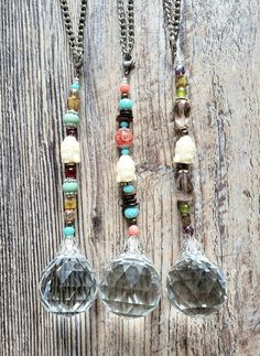 three glass ornaments are hanging from chains on a wooden surface with beads and other items