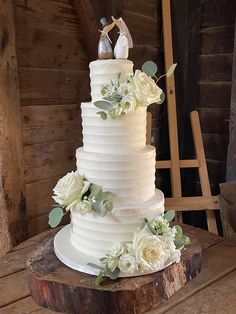 a wedding cake with white flowers and two figurines on top, sitting on a wooden table