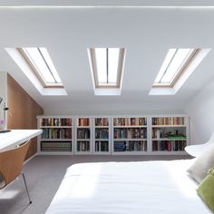 a bed sitting under two skylights in a bedroom next to a book shelf filled with books