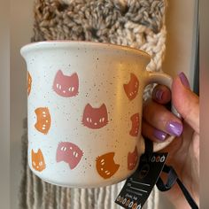 a hand holding a coffee cup with cats on it and a tag attached to the mug