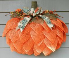 an orange mesh pumpkin hanging on the side of a house with leaves and flowers attached to it