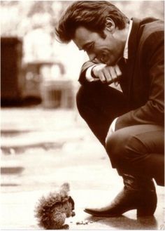 a black and white photo of a man with a squirrel on the ground next to him