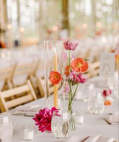 flowers in vases and candles are on the table at a wedding reception with white clothed tables