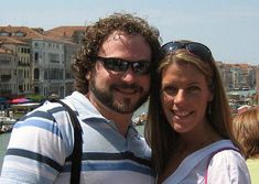 a man and woman standing next to each other in front of a body of water