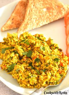 a white plate topped with scrambled eggs and sliced up tomatoes next to toasted bread