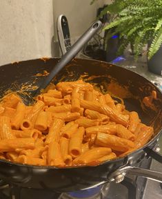 a skillet filled with pasta and sauce on top of a stove next to a plant