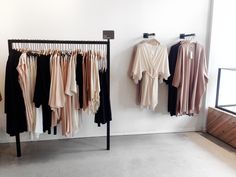 clothes are hanging on racks in a room with white walls and flooring, along with wooden furniture