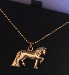 a gold necklace with a horse on it's back and a chain attached to the neck