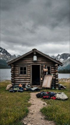 there is a small log cabin in the field with clothes and backpacks on the ground