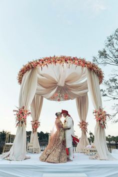 a bride and groom are standing under an arch decorated with floral decorations for their wedding ceremony