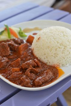 a white plate topped with meat and rice on top of a purple plastic tablecloth