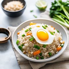 rice with peas, carrots and an egg on top in a white bowl next to chopsticks