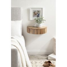 a bedroom with white walls and a small wooden shelf on the wall next to a bed