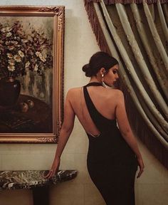 a woman standing in front of a painting wearing a black dress with back cutouts