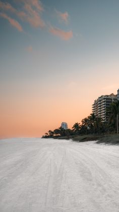 the beach is covered in white sand and palm trees as the sun sets behind buildings