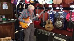 an older man is playing his guitar in a music store with guitars on the wall behind him